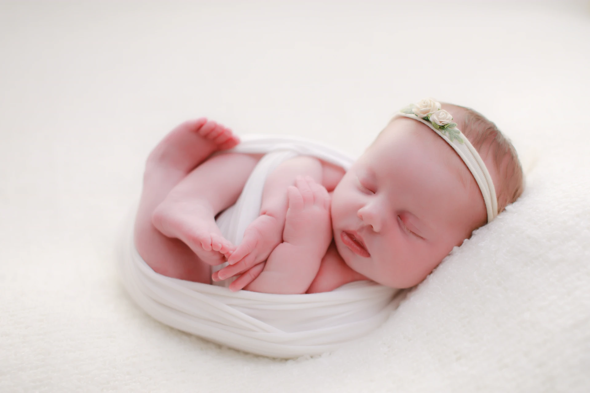 Sleeping newborn wrapped in white with a floral headband
