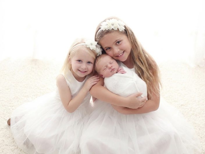 Two sisters holding a newborn baby in a sibling portrait at Sweetlife Photography North Lakes