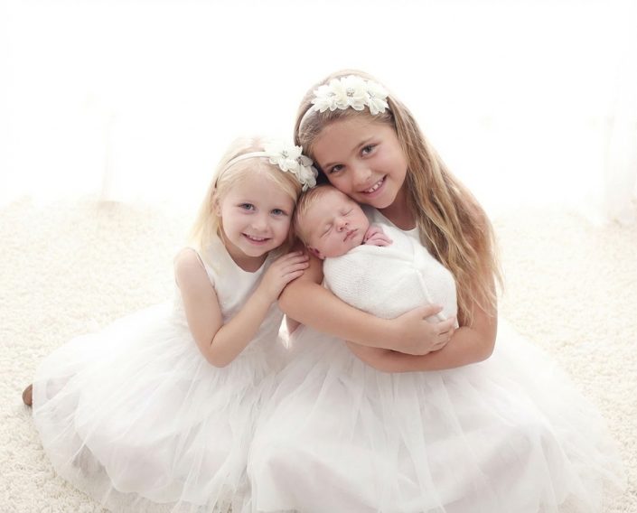 Two sisters holding a newborn baby in a sibling portrait at Sweetlife Photography North Lakes