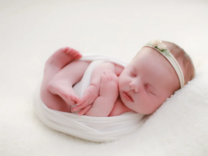Sleeping newborn girl wrapped in white with a floral headband at Sweetlife Photography North Lakes