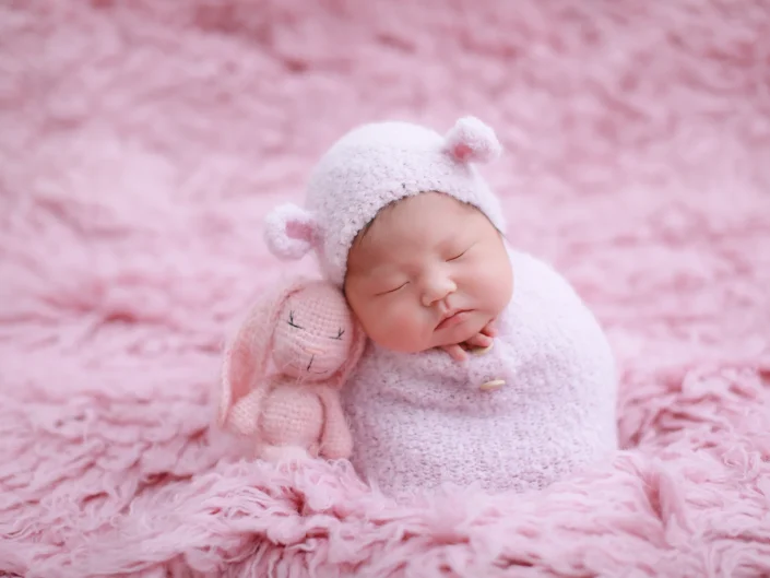 Sleeping newborn in a pink teddy bonnet beside a pink knitted toy at Sweetlife Photography North Lakes