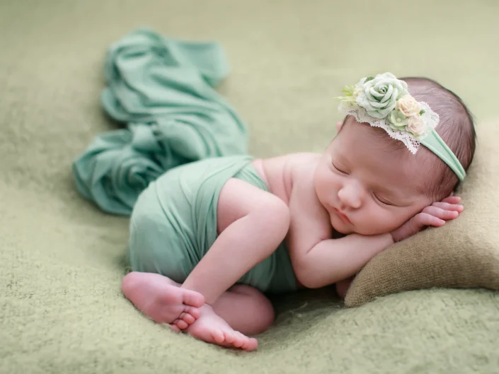 Sleeping newborn in a mint wrap with a floral headband on a green blanket at Sweetlife Photography North Lakes