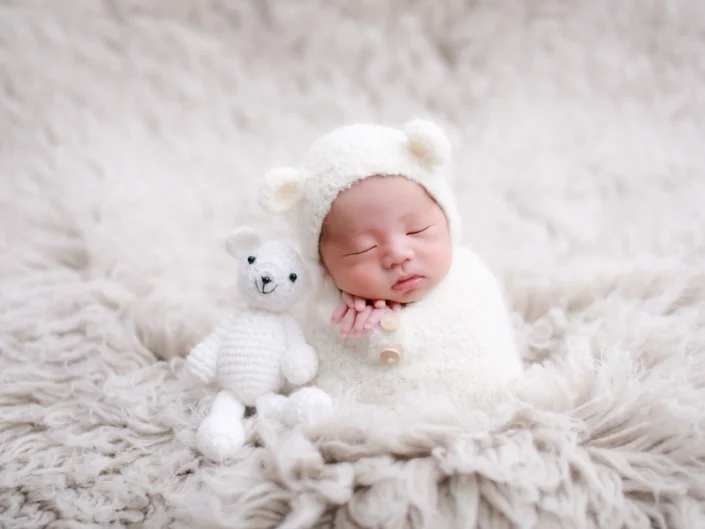 Sleeping newborn in a white teddy bonnet beside a knitted bear at Sweetlife Photography North Lakes