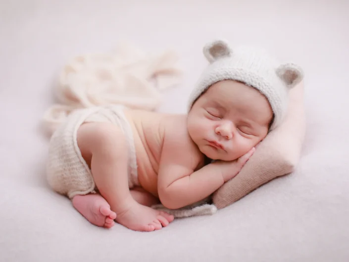 Sleeping newborn in a white knit bear bonnet resting on a blush pillow at Sweetlife Photography North Lakes