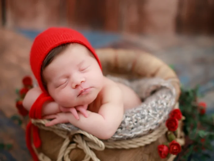 Sleeping newborn in a red bonnet in a rustic basket with red roses at Sweetlife Photography North Lakes