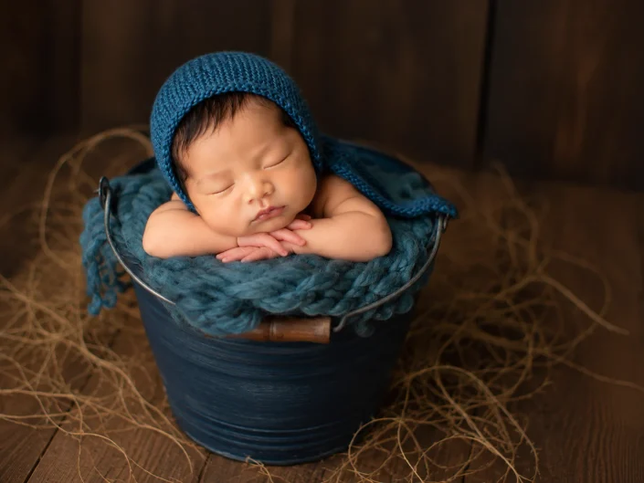 Sleeping newborn in a deep blue wrap in a blue bucket at Sweetlife Photography North Lakes