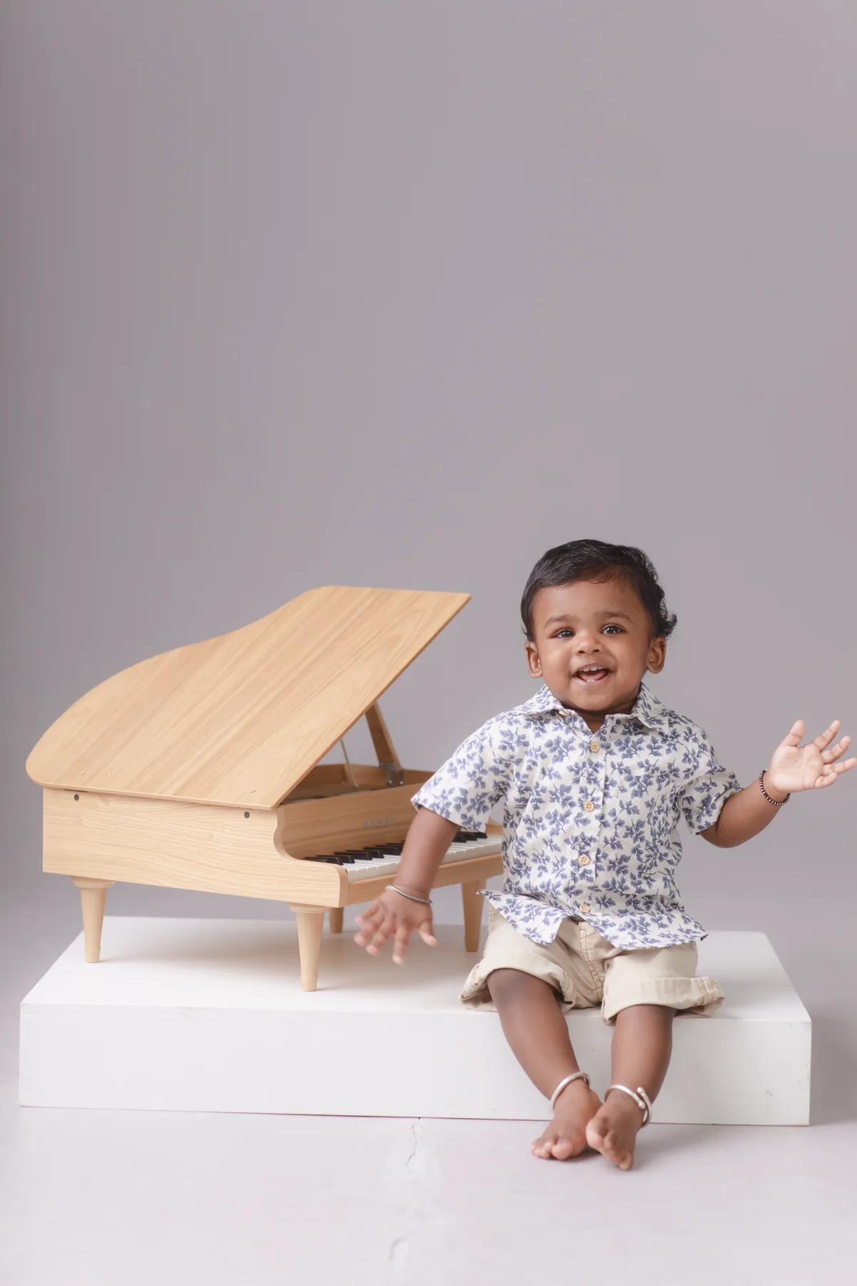 Smiling baby boy seated beside a wooden toy piano during a studio milestone portrait session