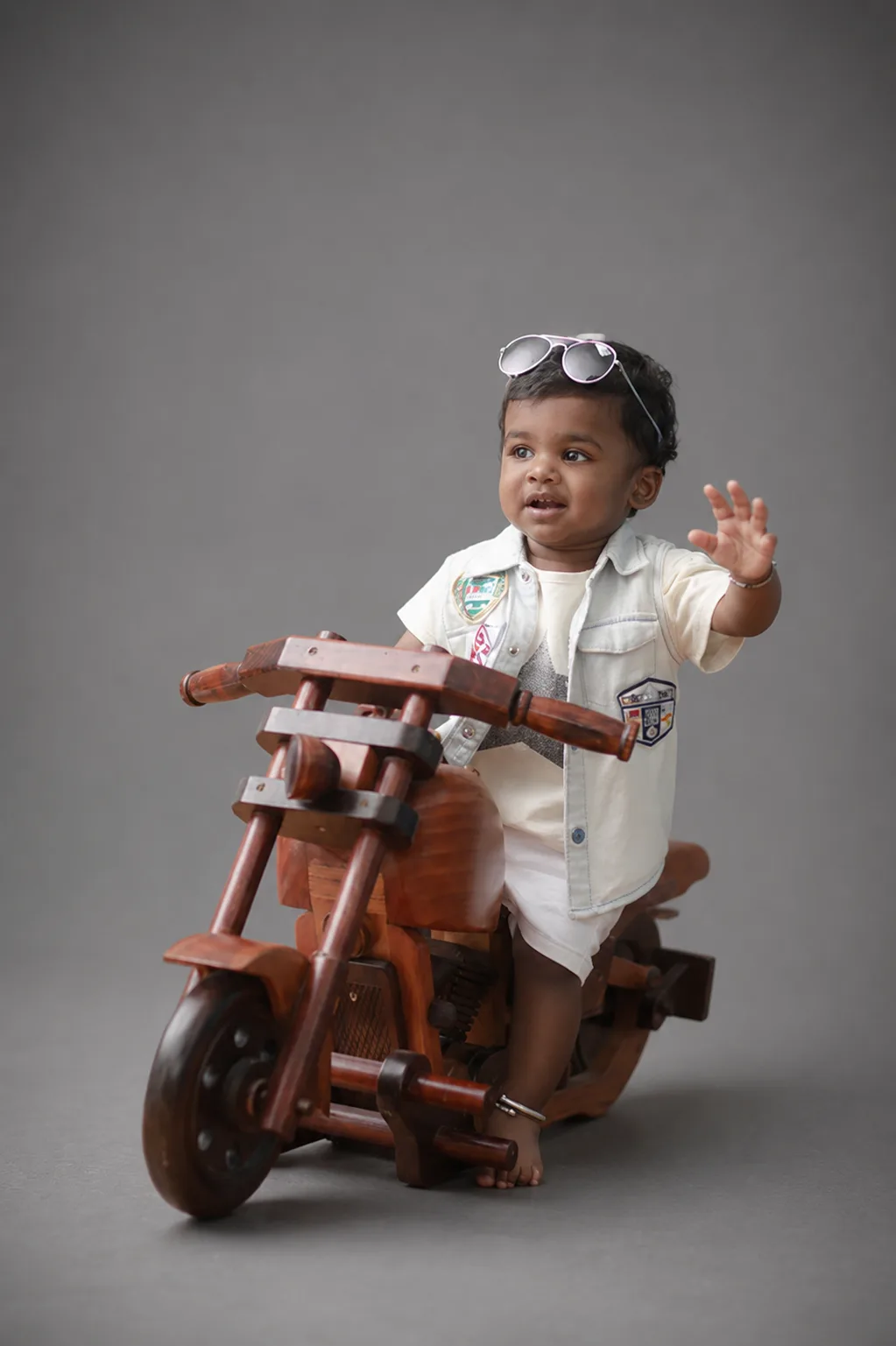 Young child wearing sunglasses and posing on a wooden toy motorcycle